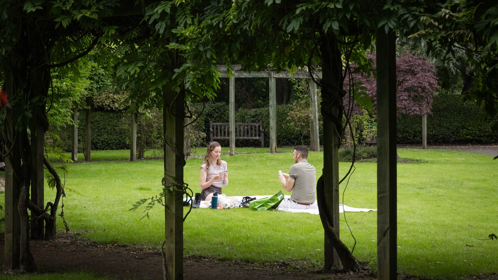 A couple having a picnic on the grass among trees in Fletcher Moss Gardens, Manchester